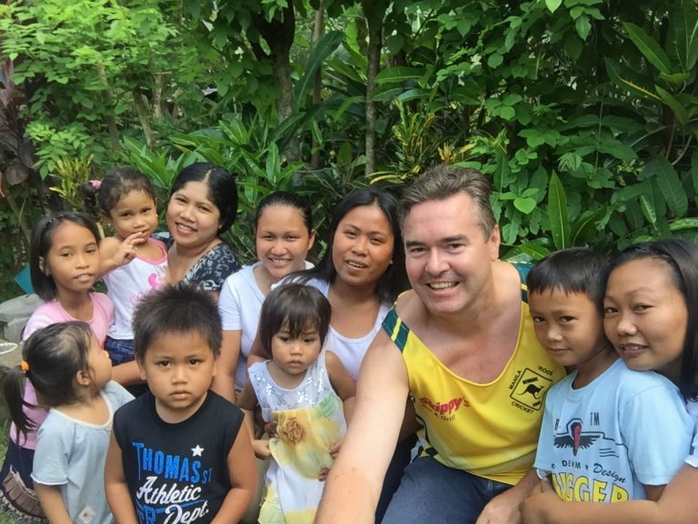 Dezza posing for a selfie with a group of Filipino friends and children in a tropical garden