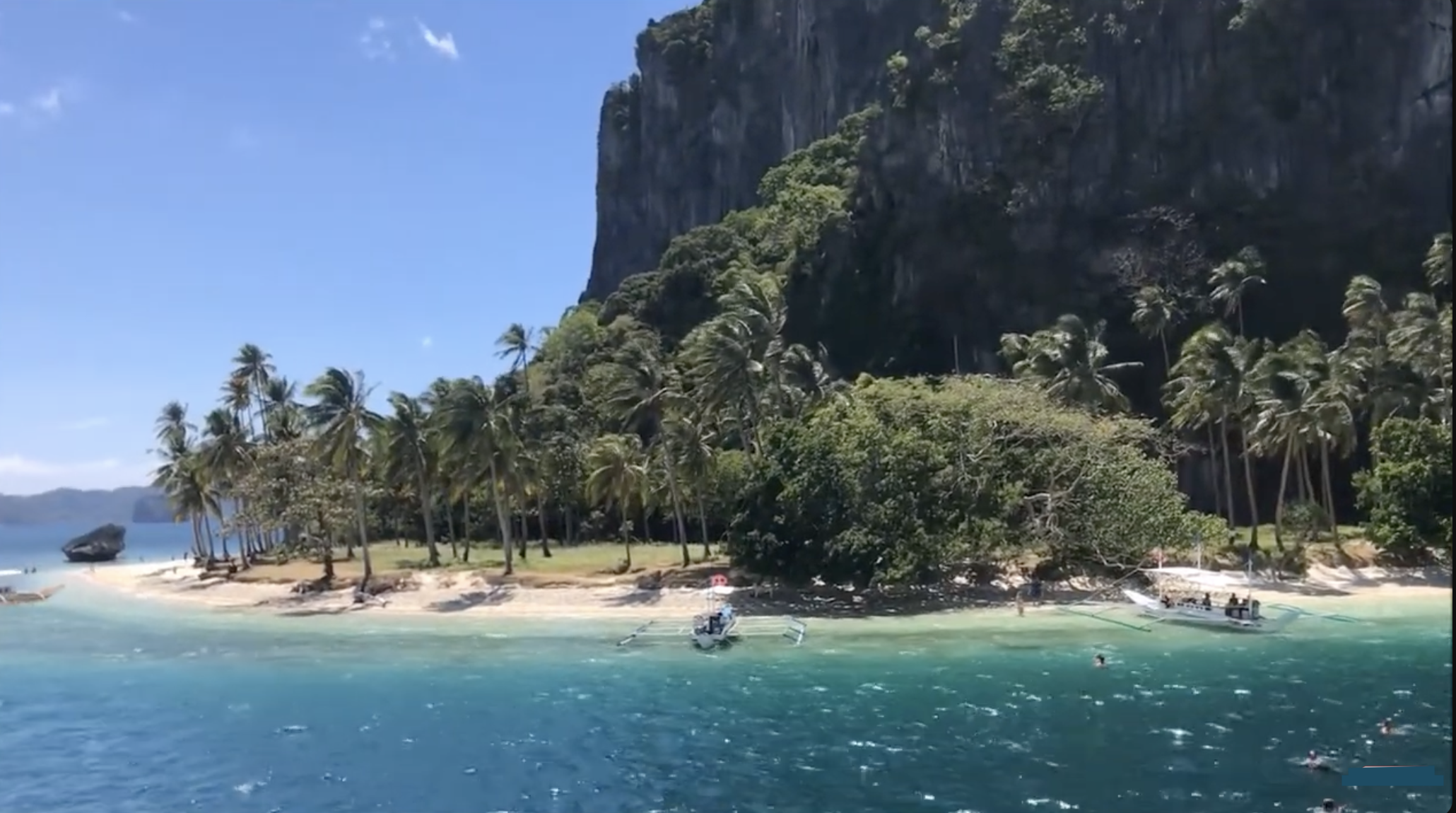Pinagbuyutan Island, El Nido, with palm trees, a white sand beach and boats anchored in turquoise water