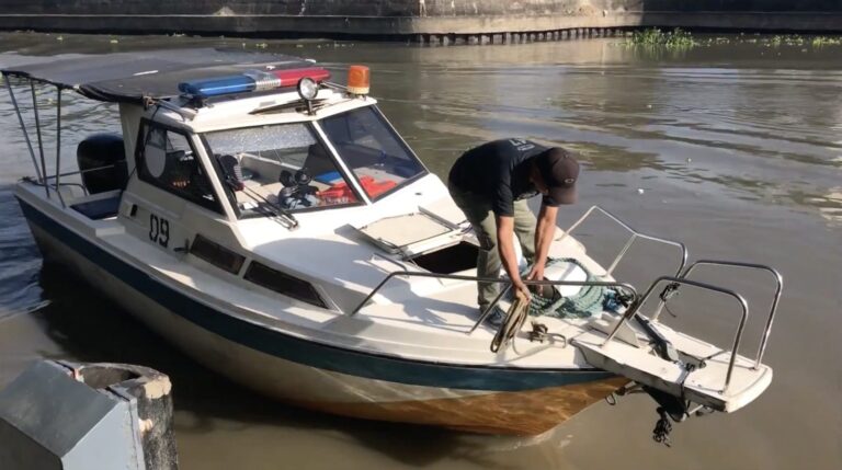 Crew member coiling a rope on the bow of a small boat on the Pasig River