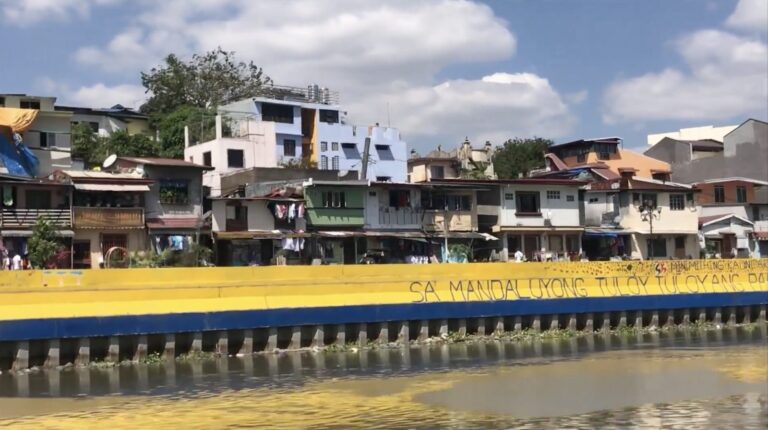 Riverside houses behind a yellow and blue seawall on the Pasig River