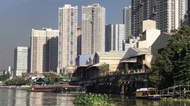 Tall residential towers behind old riverside warehouses on the Pasig River