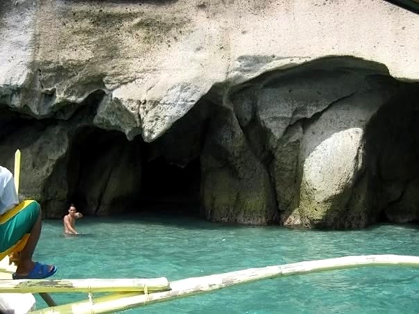 Boat outrigger in front of a Ramos Caves sea cave with clear turquoise water, Nasugbu, Batangas