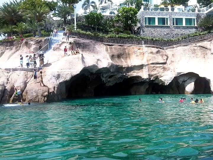 Swimmers in turquoise water below the Ramos Caves rock arches near Panutsutan Beach, Nasugbu