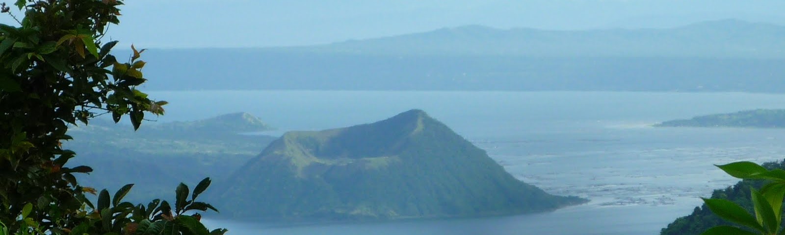 View of Taal Volcano and Taal Lake from the Tagaytay ridge, framed by trees