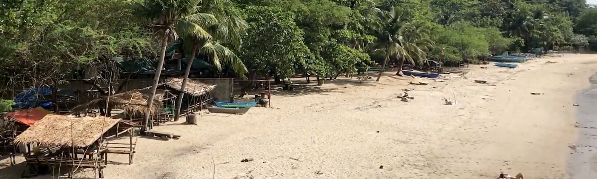 Panutsutan Beach in Nasugbu, Batangas, with nipa huts, palms and a forested hill behind a long stretch of sand