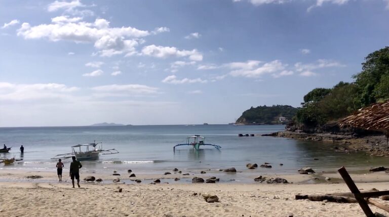 Panutsutan Beach with bancas in shallow water and a headland in the distance
