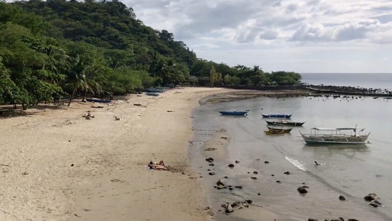 Long curve of sand at Panutsutan Beach with bancas moored in calm water