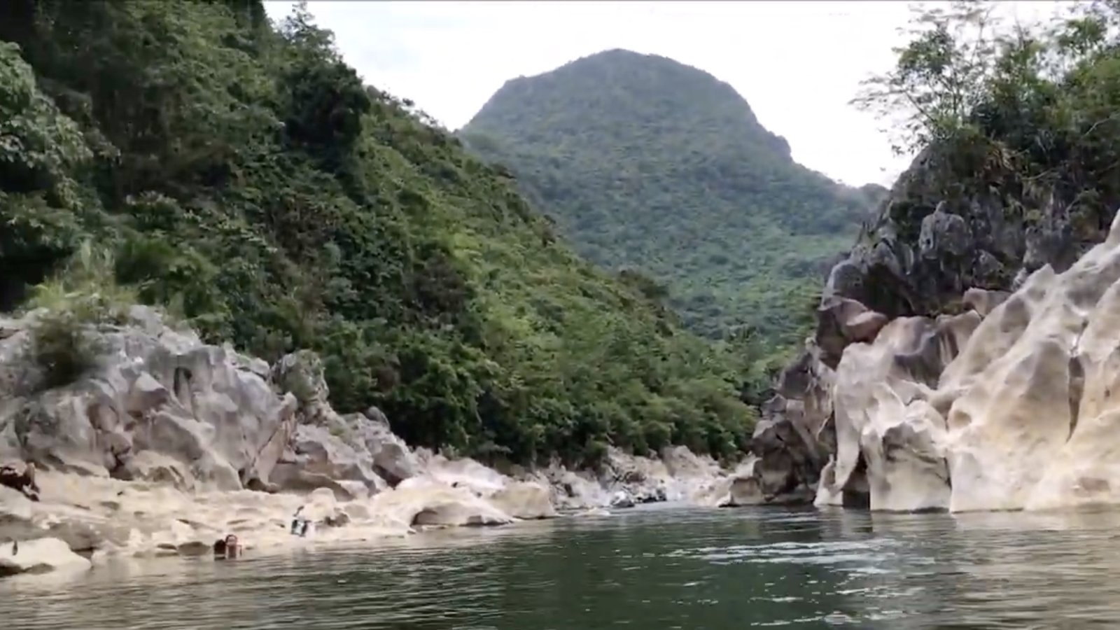 Swimmers beside pale limestone rocks in a green river gorge at Tinipak River, Rizal